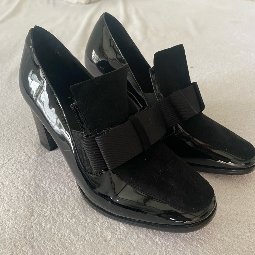 Patent leather and suede black dress shoes with red sole and bow.